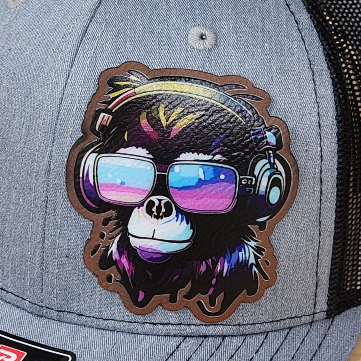 Gray cap with a colorful monkey design wearing sunglasses and headphones on a black background