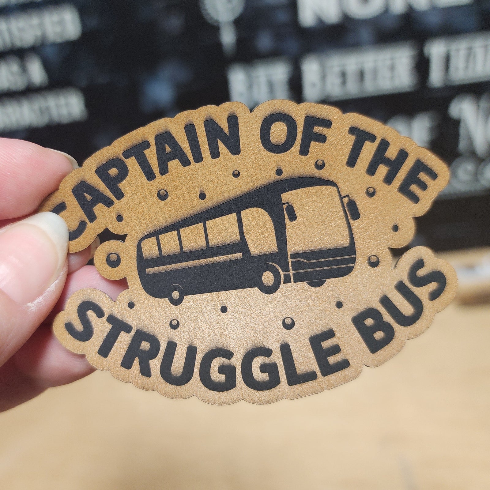 Patch with 'Captain of the Struggle Bus' text and graphic held by a hand.