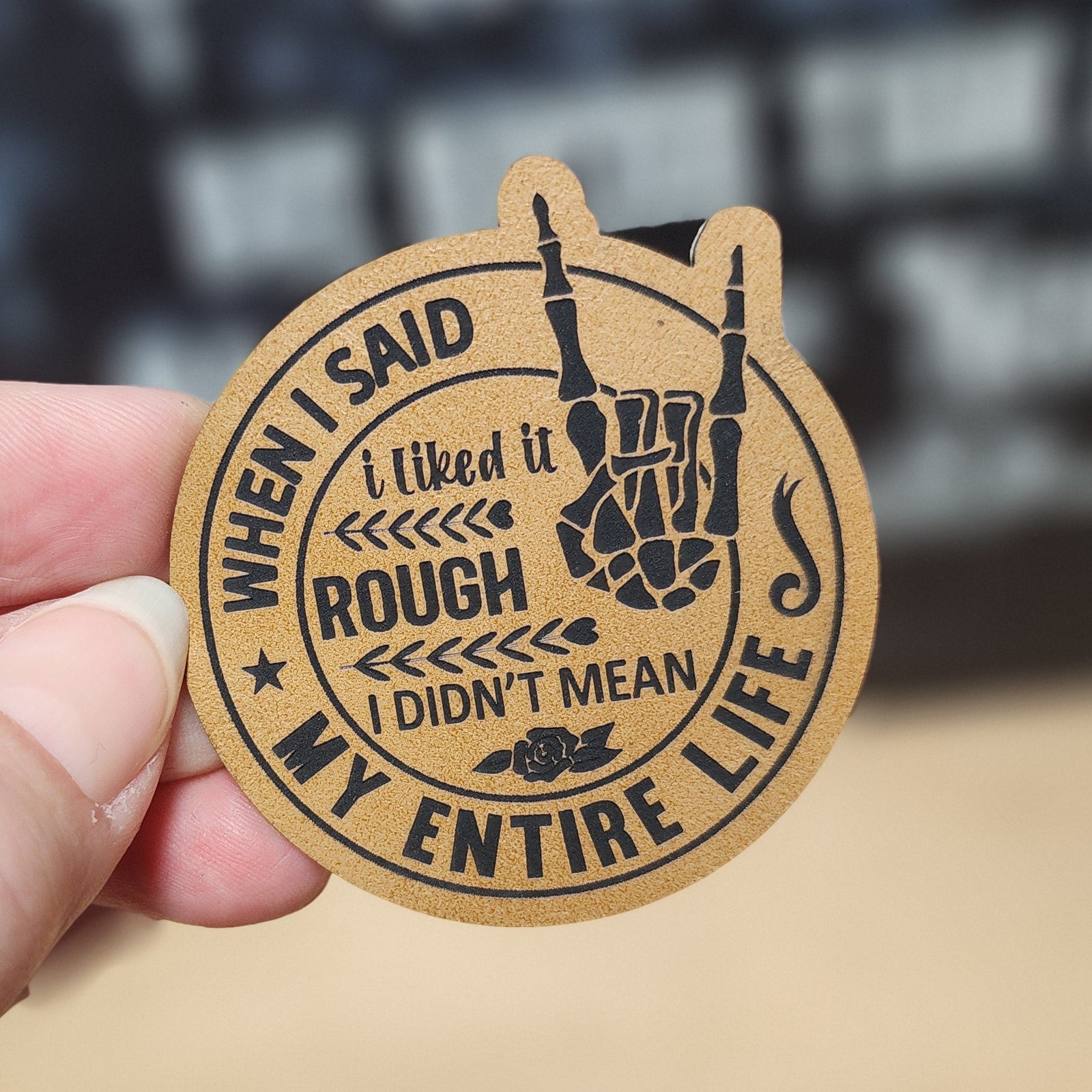 Hand holding a leatherette round patch with text and design, blurred background