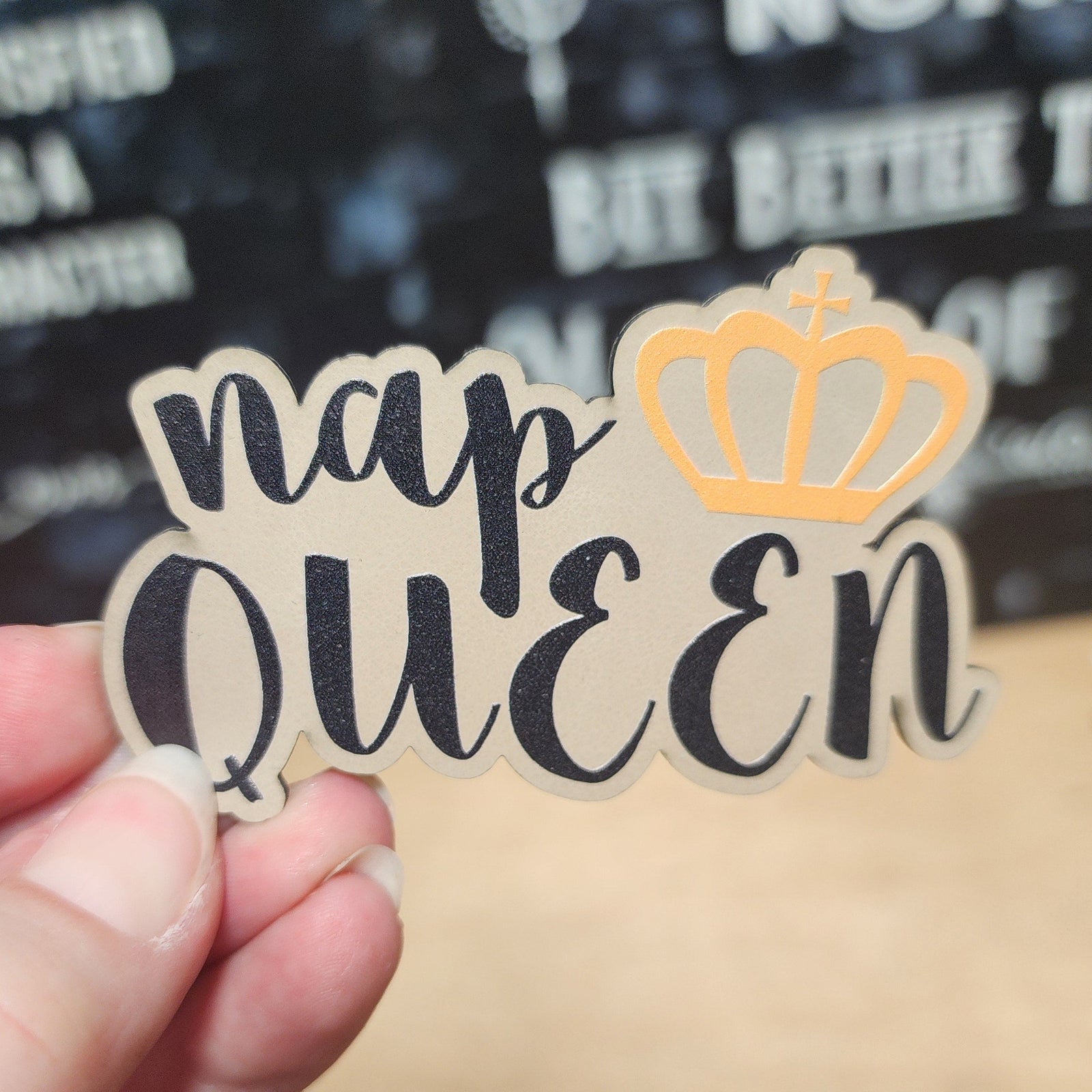 Hand holding a 'nap queen' patch with a crown on a blurred background