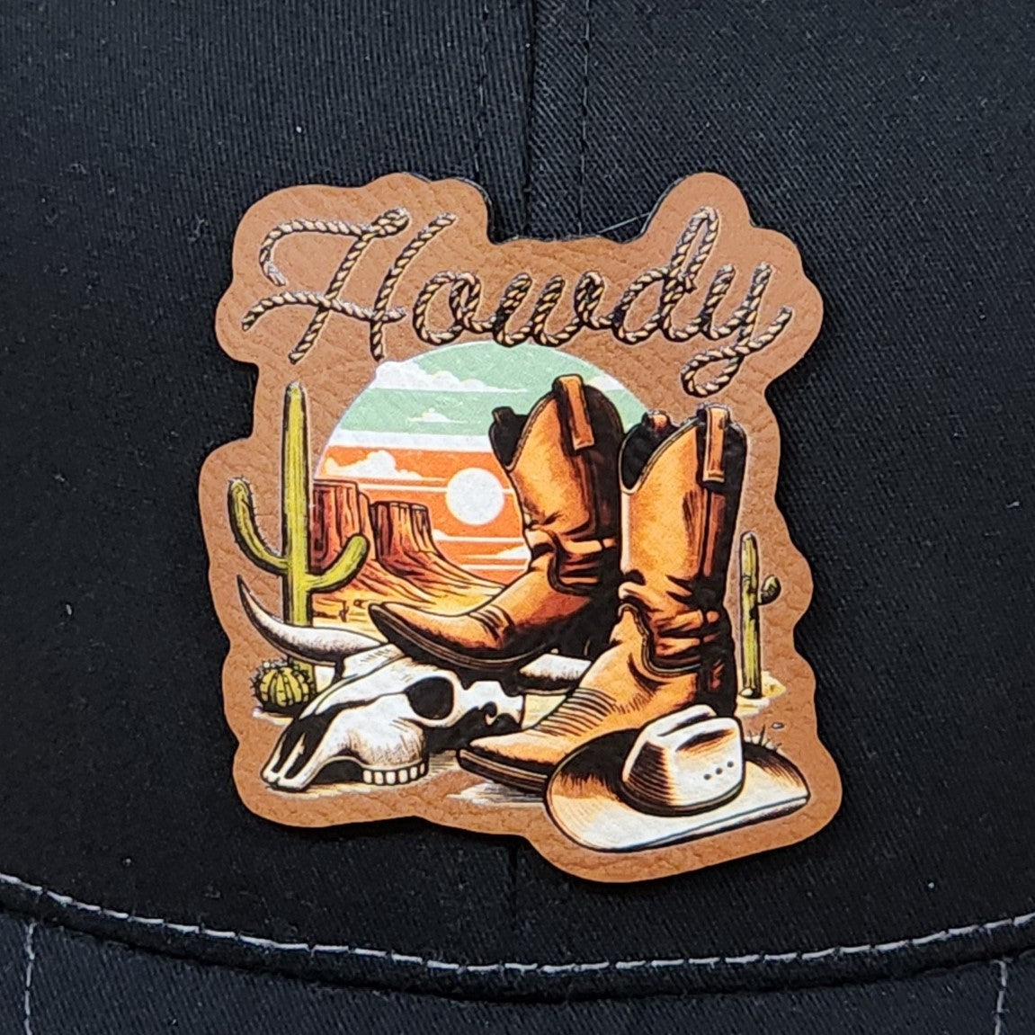 Cowboy leatherette hat patch featuring boots, cactus, and sunset scenery, perfect for western attire.
