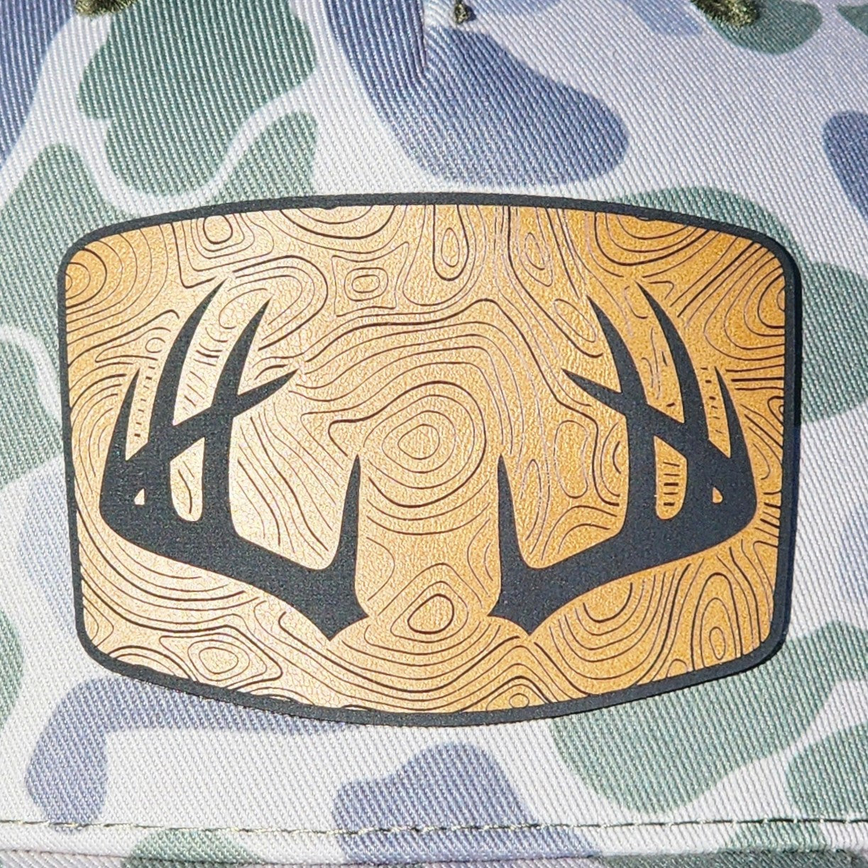 Camo leatherette hat patch featuring intricate antlers and a wood grain design for outdoor enthusiasts.