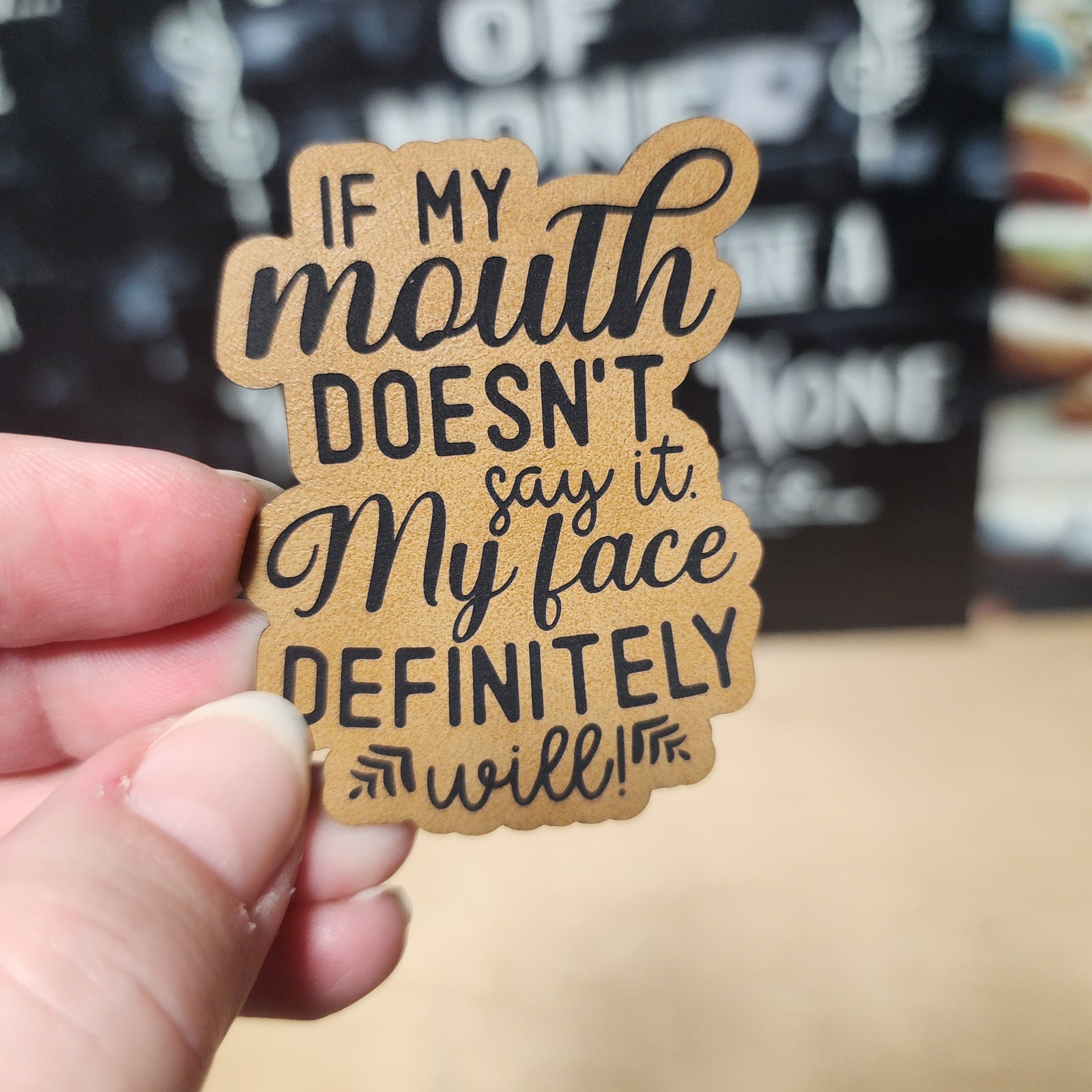 Funny leatherette hat patch with saying 'If my mouth doesn't say it, my face definitely will!' for humor lovers.