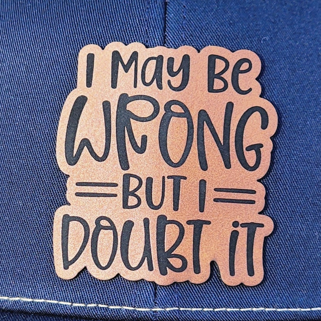 Stylish leatherette hat patch with witty saying 'I MAY BE WRONG BUT I DOUBT IT' for trendy caps and accessories.