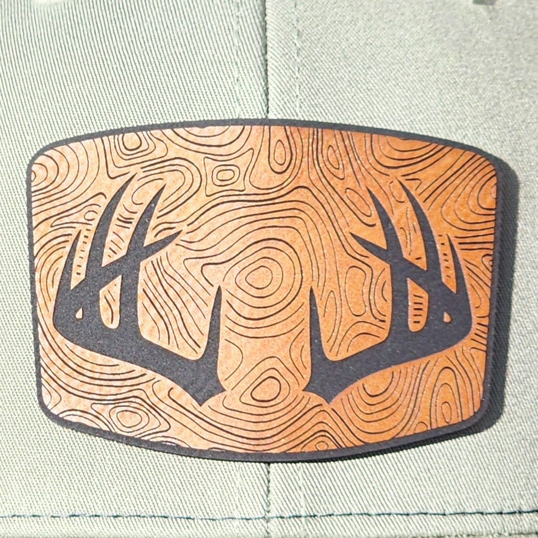 Outdoor leatherette hat patch featuring antlers and a woodgrain design, perfect for hunting enthusiasts.