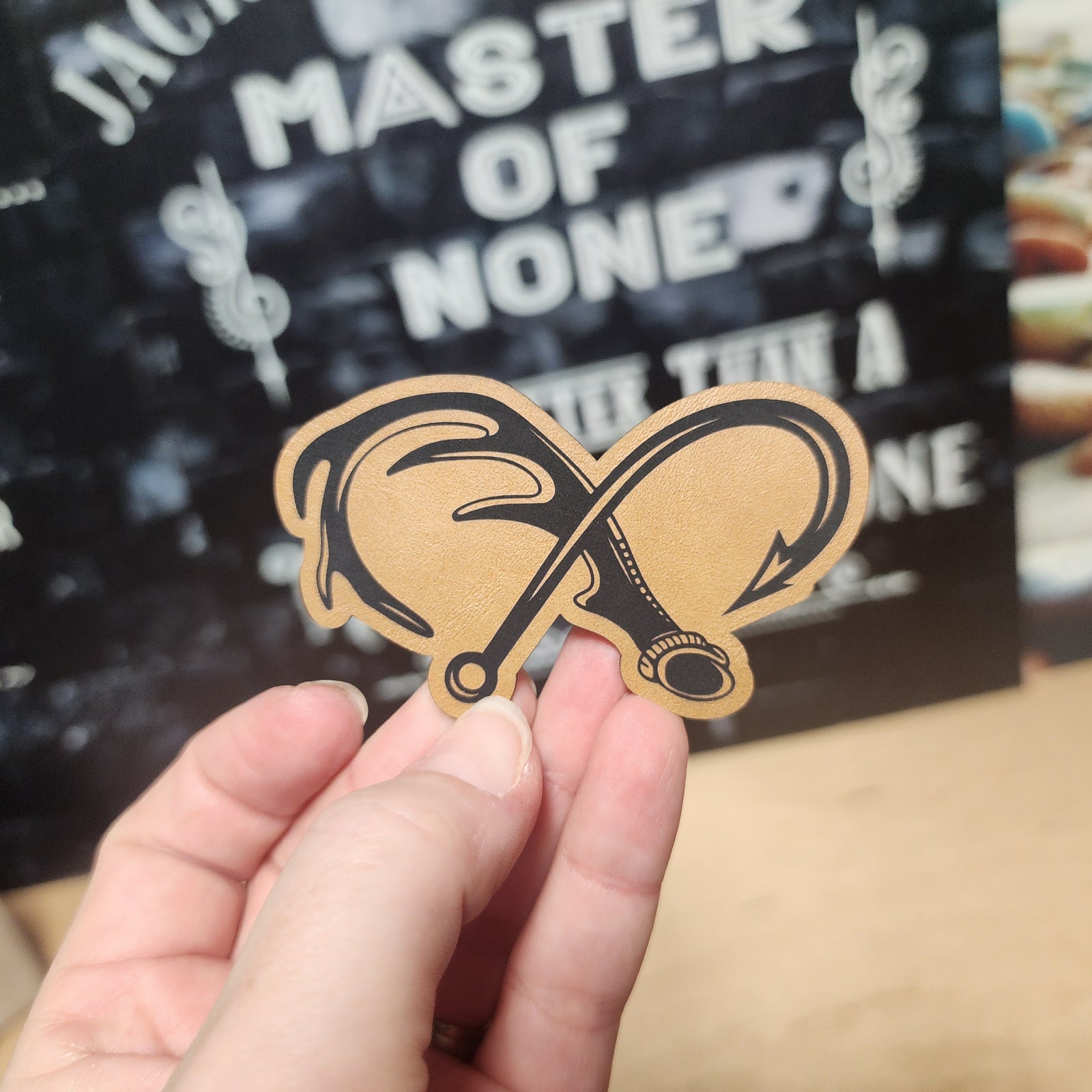 Master of None leatherette hat patch featuring crossed fishing hooks, perfect for anglers and outdoor enthusiasts.