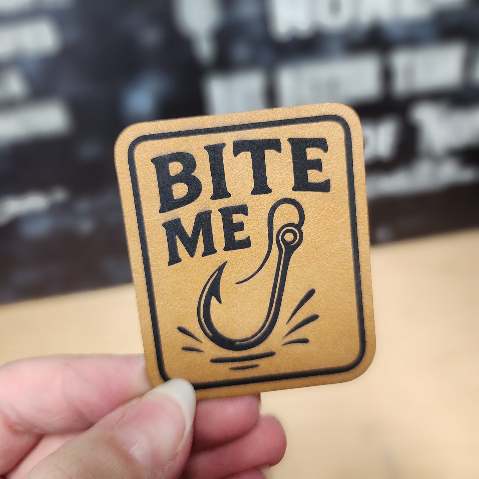 Bite Me fishing leatherette hat patch with a fishhook design, perfect for fishing enthusiasts and outdoor lovers.