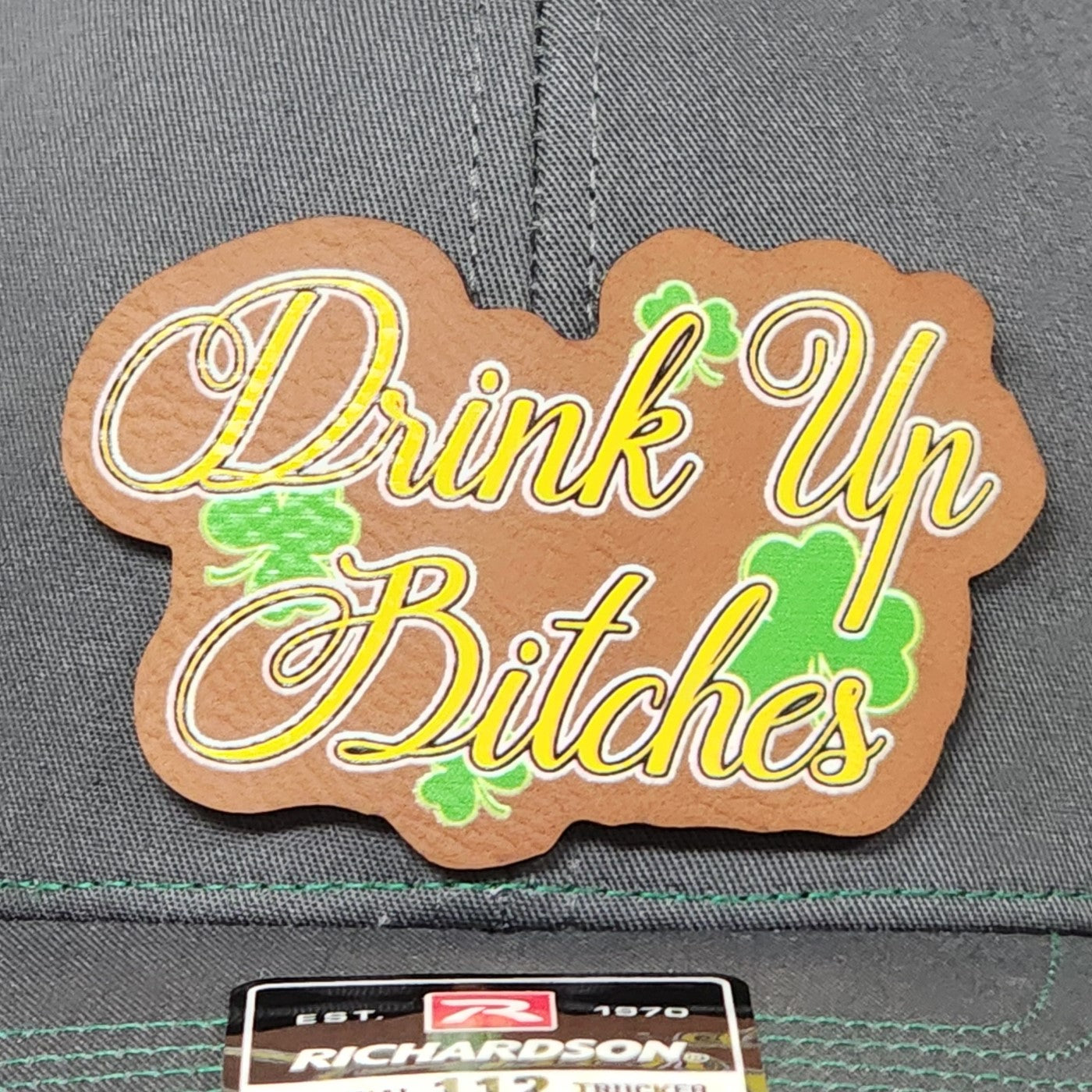 St. Patrick's Day leatherette hat patch saying 'Drink Up Bitches' with shamrocks, perfect for festive celebrations.