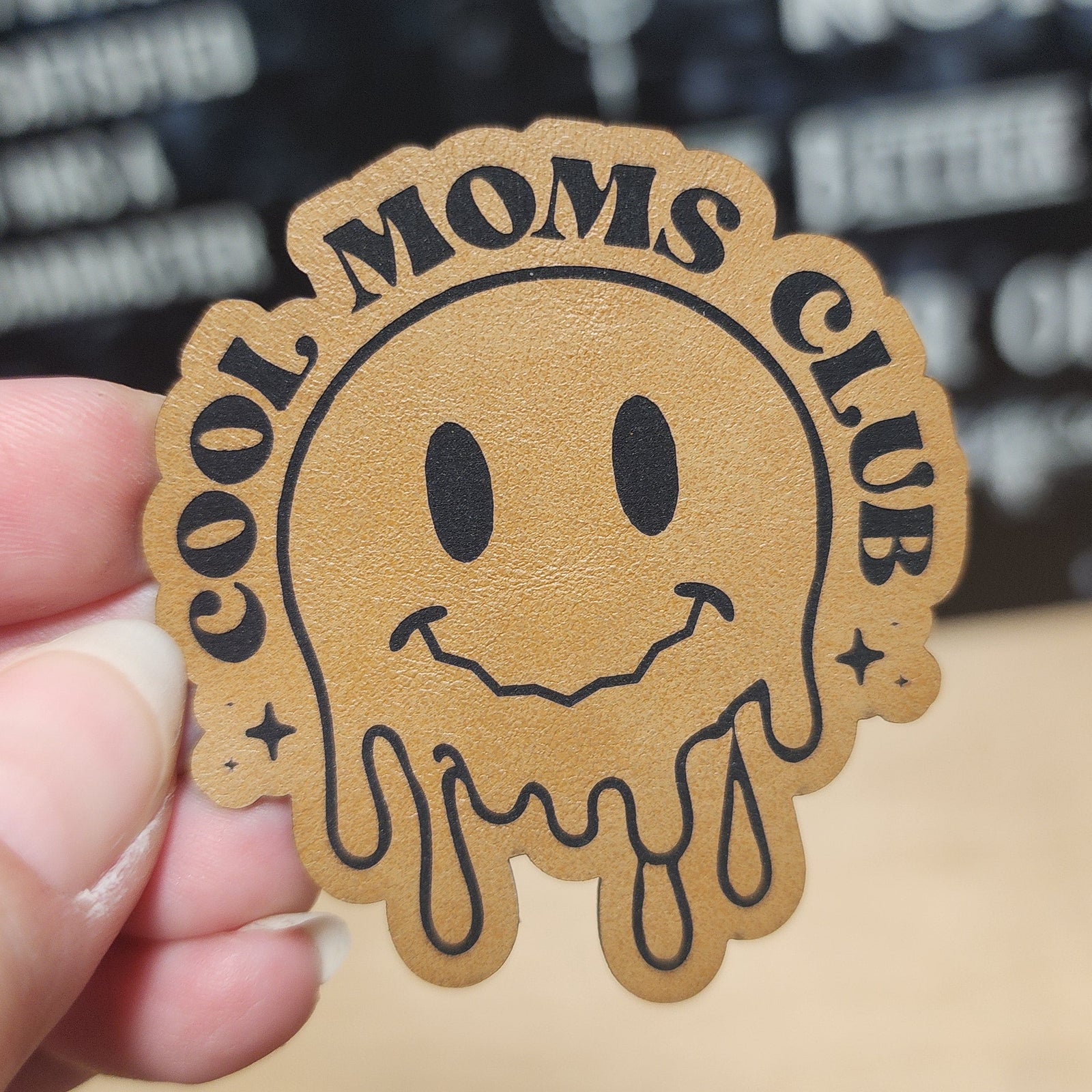 Cool Moms Club leatherette hat patch with smiling melted smiley face for trendy accessories and gifts.