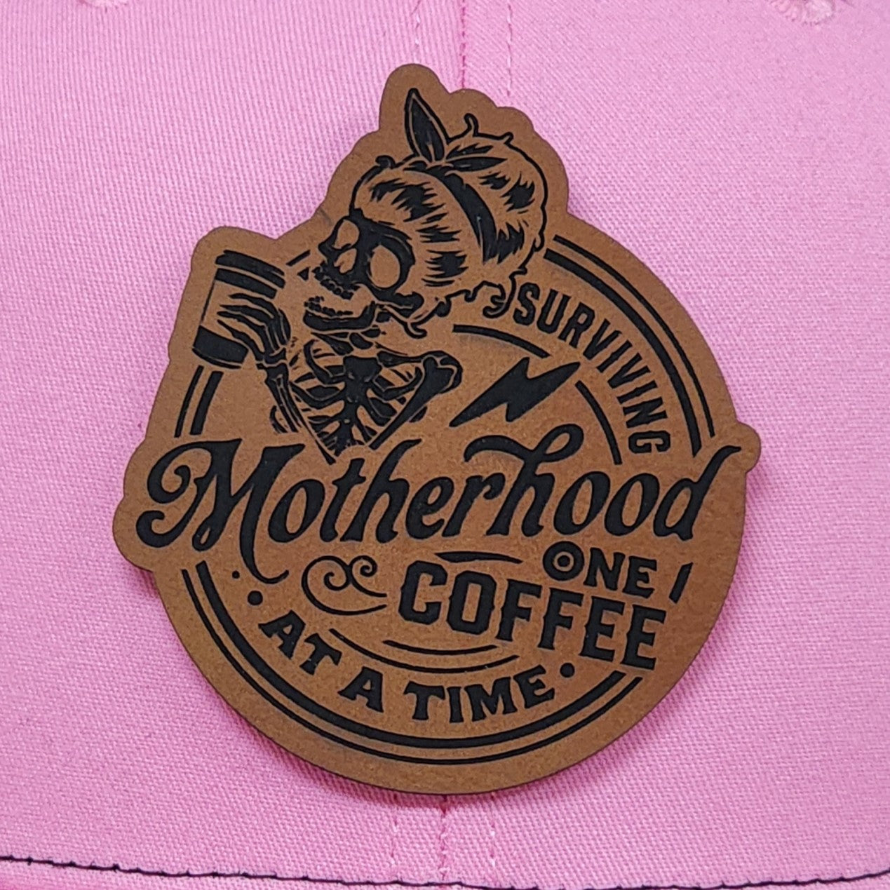 Motherhood coffee hat patch, skeleton design, leatherette cap accessory for coffee lovers and moms, pink background.
