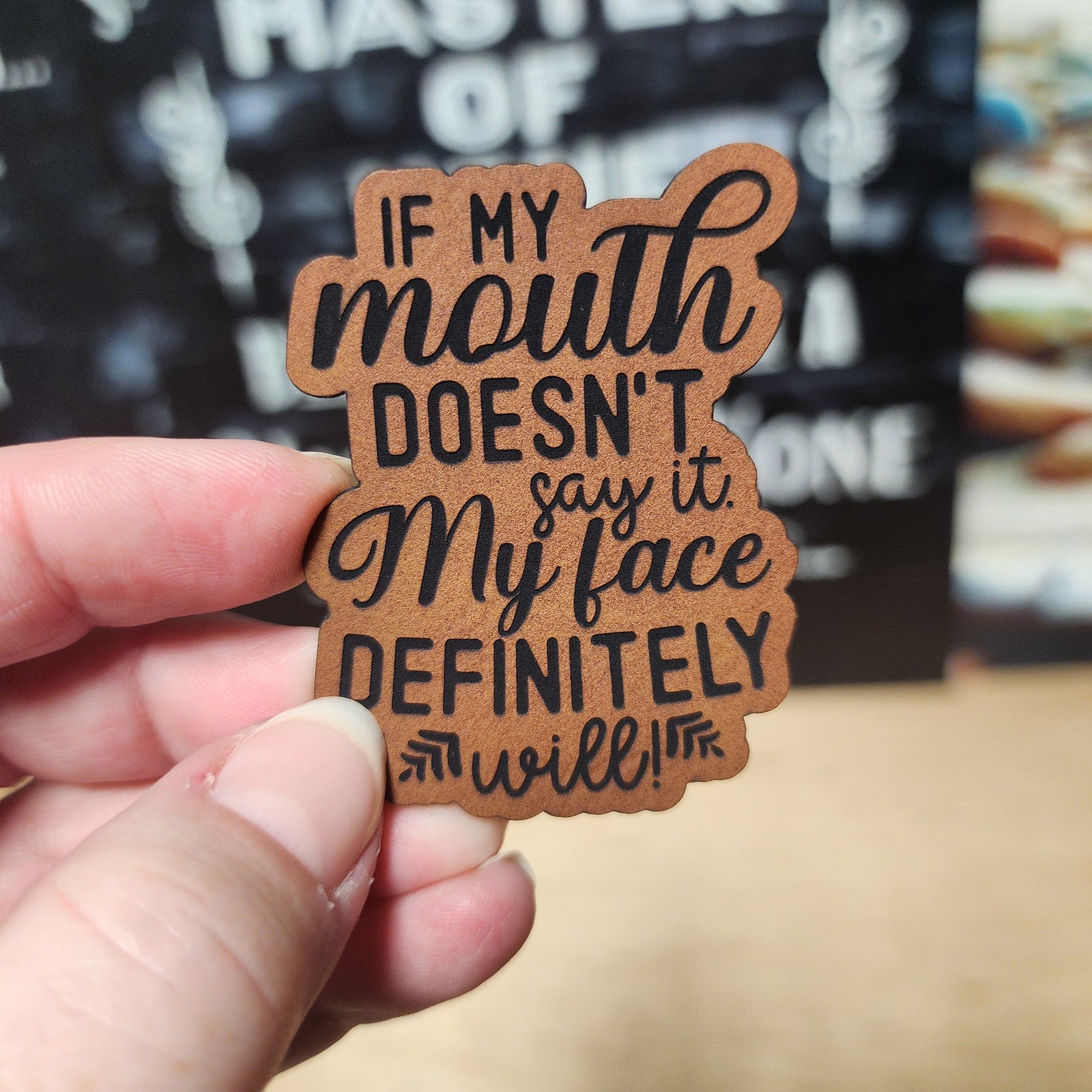 Humorous leatherette hat patch saying, 'If my mouth doesn't say it, my face definitely will!' for unique hats.