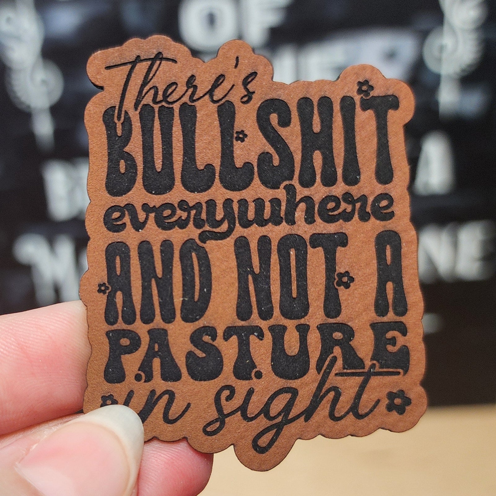 Leatherette hat patch with humorous quote saying 'There's bullshit everywhere and not a pasture in sight'.