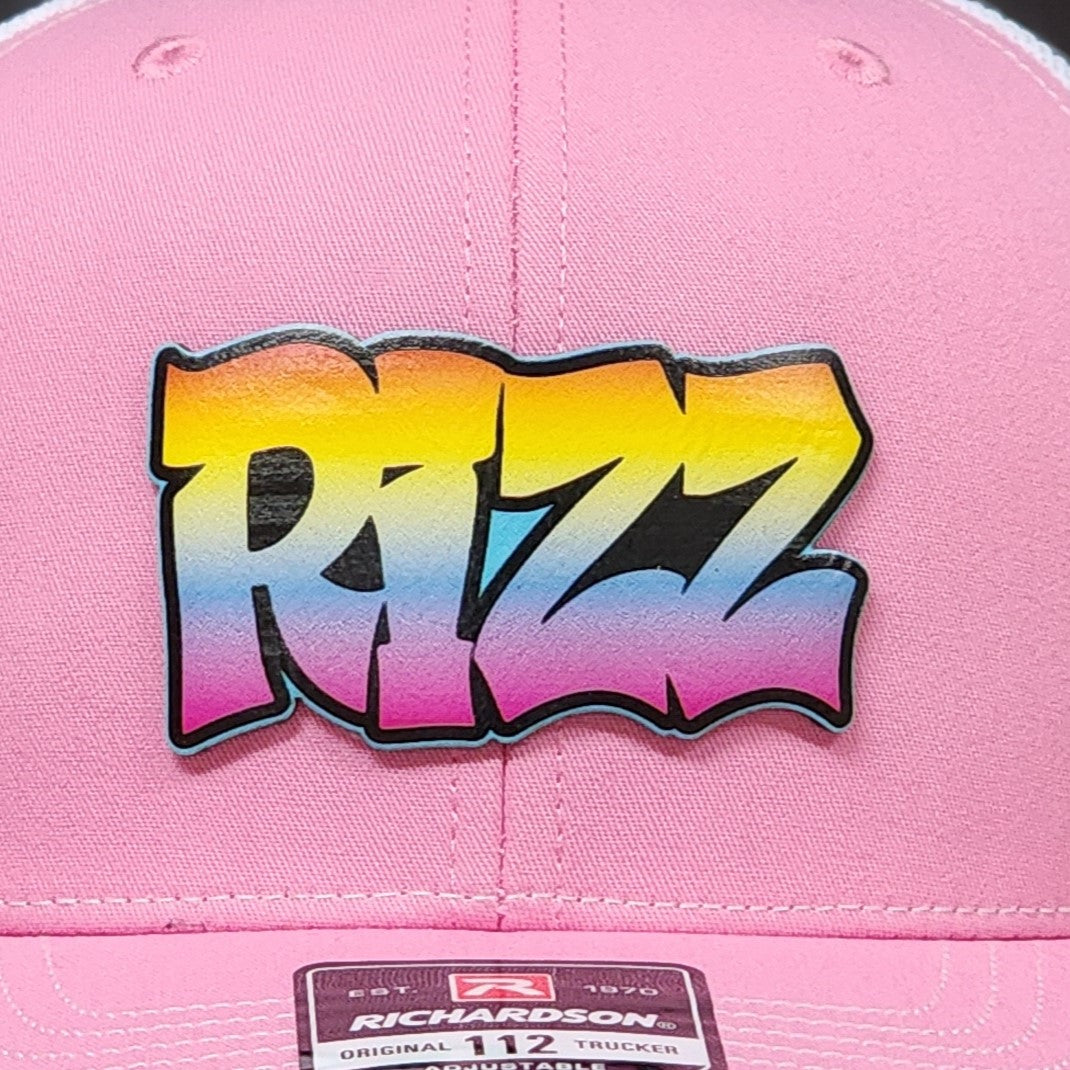Custom leatherette hat patch featuring vibrant 'RIZZ' graffiti design on a pink trucker cap for trendy wear.