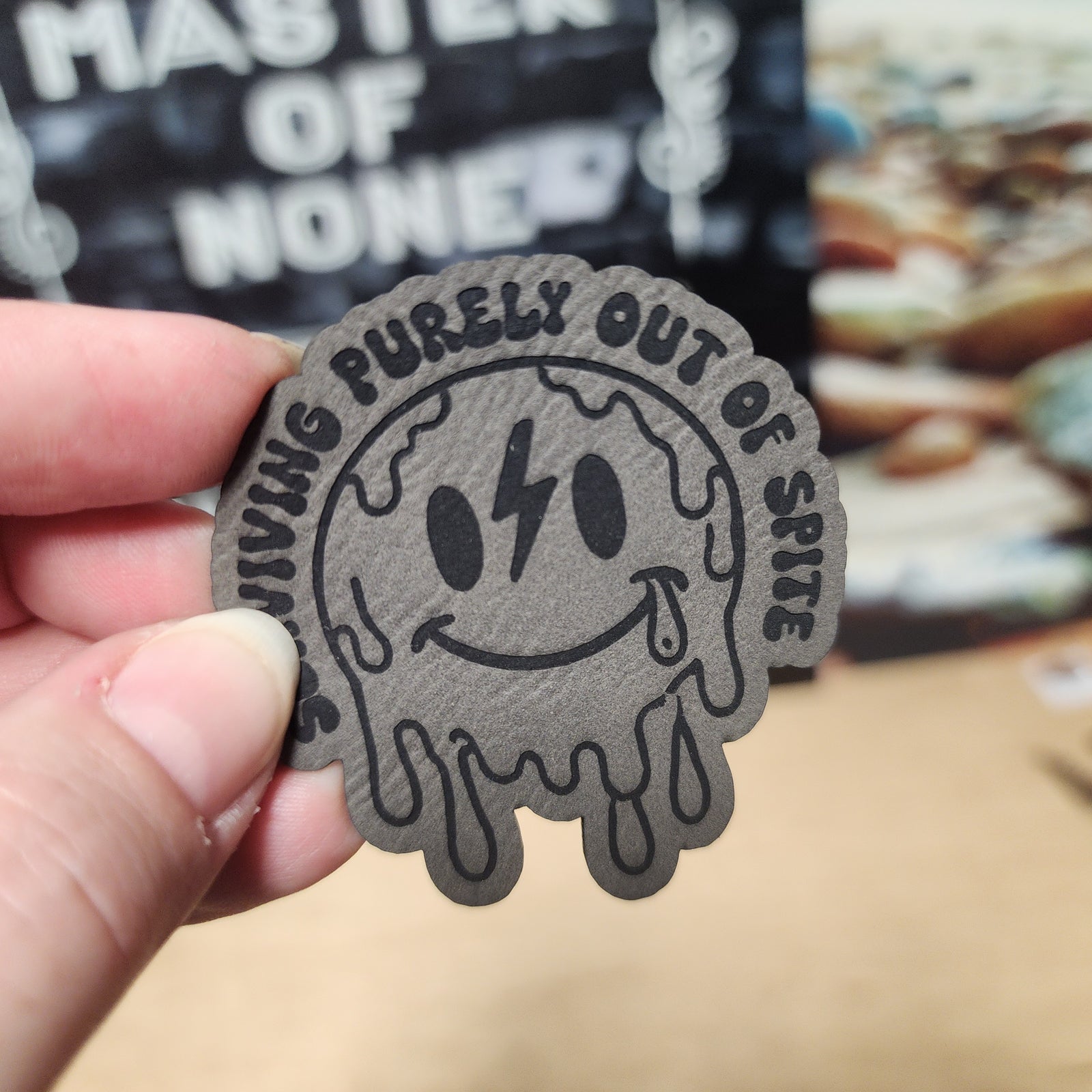 Funny leatherette hat patch featuring a melting smiley face with the phrase 'Living Purely Out of Spite'.