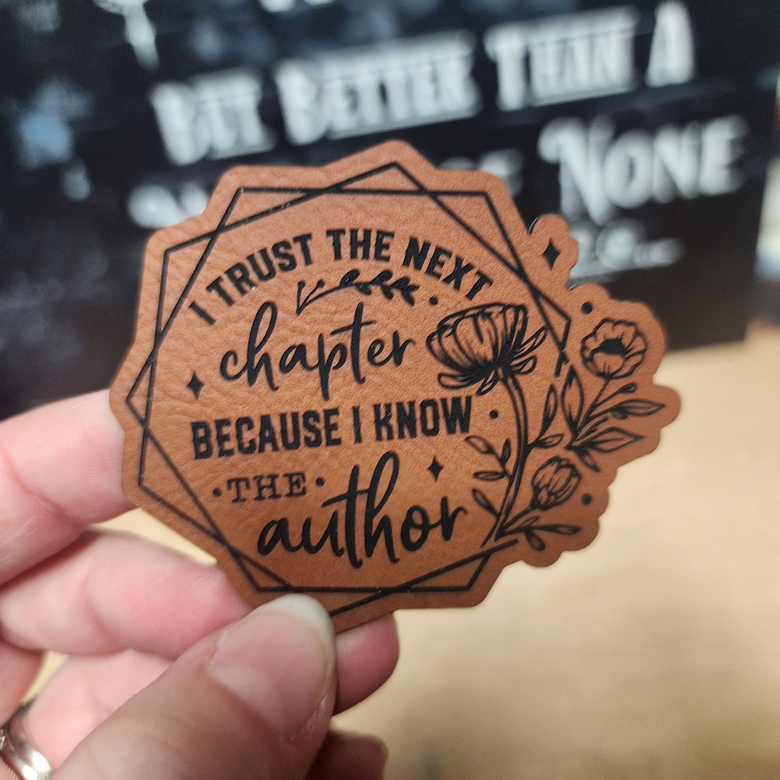 Inspirational leatherette hat patch, 'Trust the Next Chapter,' perfect for book lovers and creative spirits.