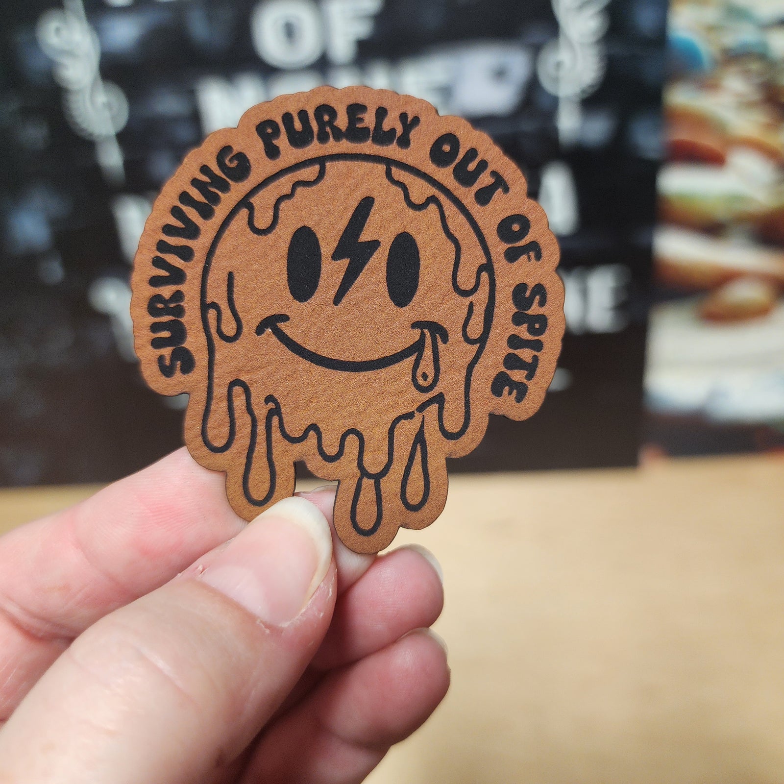 Surviving Purely Out of Spite leatherette hat patch, quirky smiley face design with drips for unique accessories.