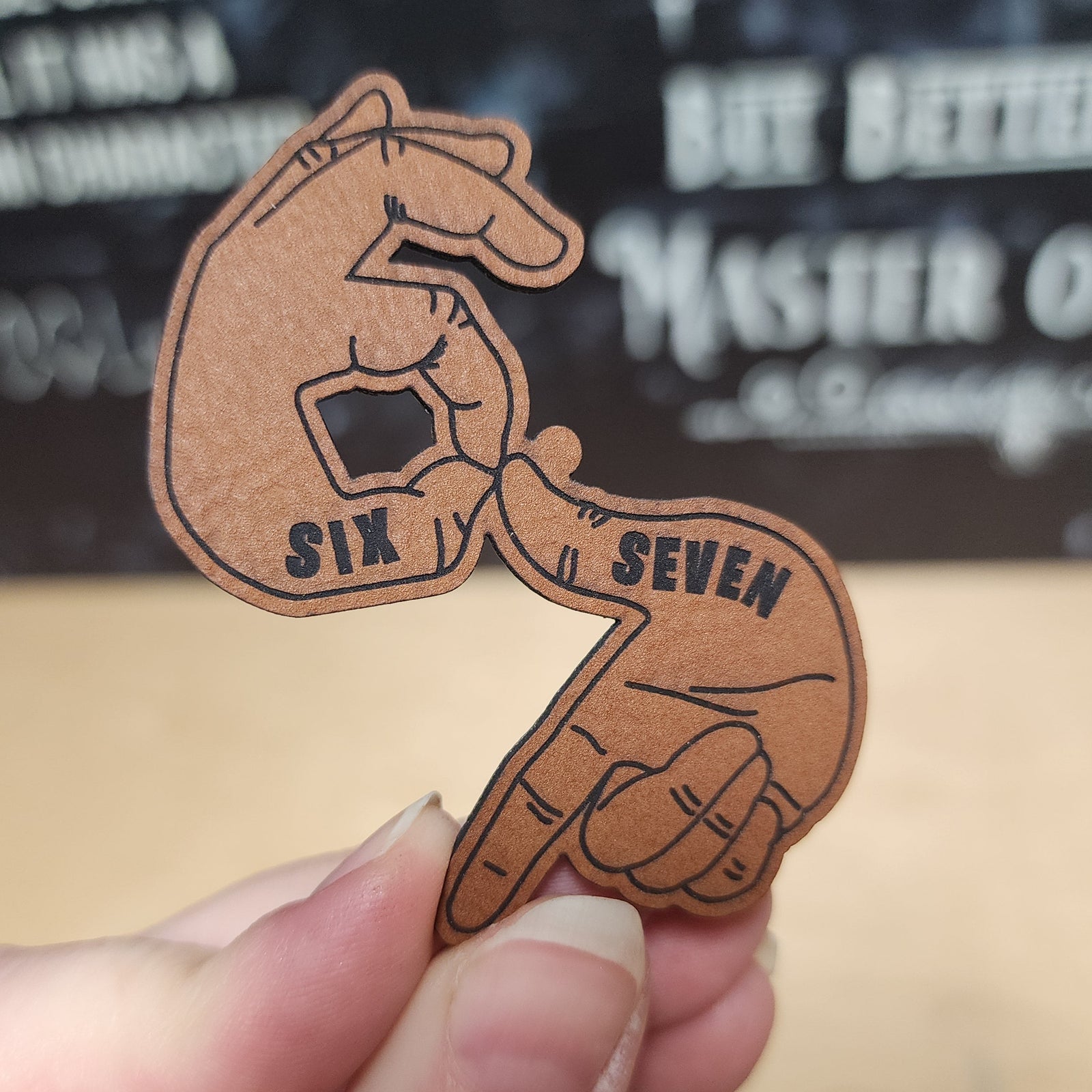 Leatherette hat patch featuring hands making 'Six' and 'Seven' gestures, perfect for unique apparel and accessories.