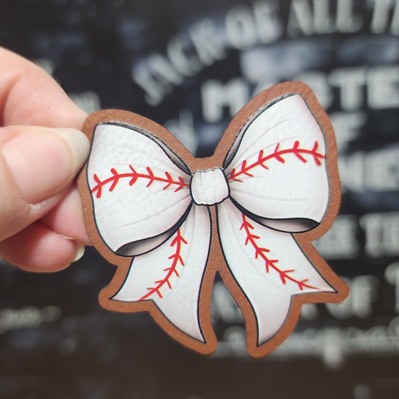Baseball-themed leatherette patch featuring a white bow design with red stitching, perfect for sports fans.