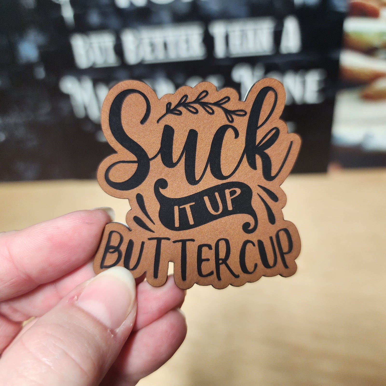 Quirky leatherette hat patch with 'Suck It Up Buttercup' phrase, perfect for humor-loving hat enthusiasts.