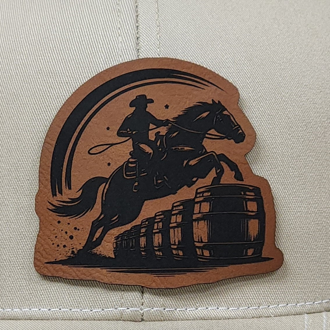 Cowboy leatherette hat patch featuring a horse rider jumping over barrels, perfect for western fashion enthusiasts.