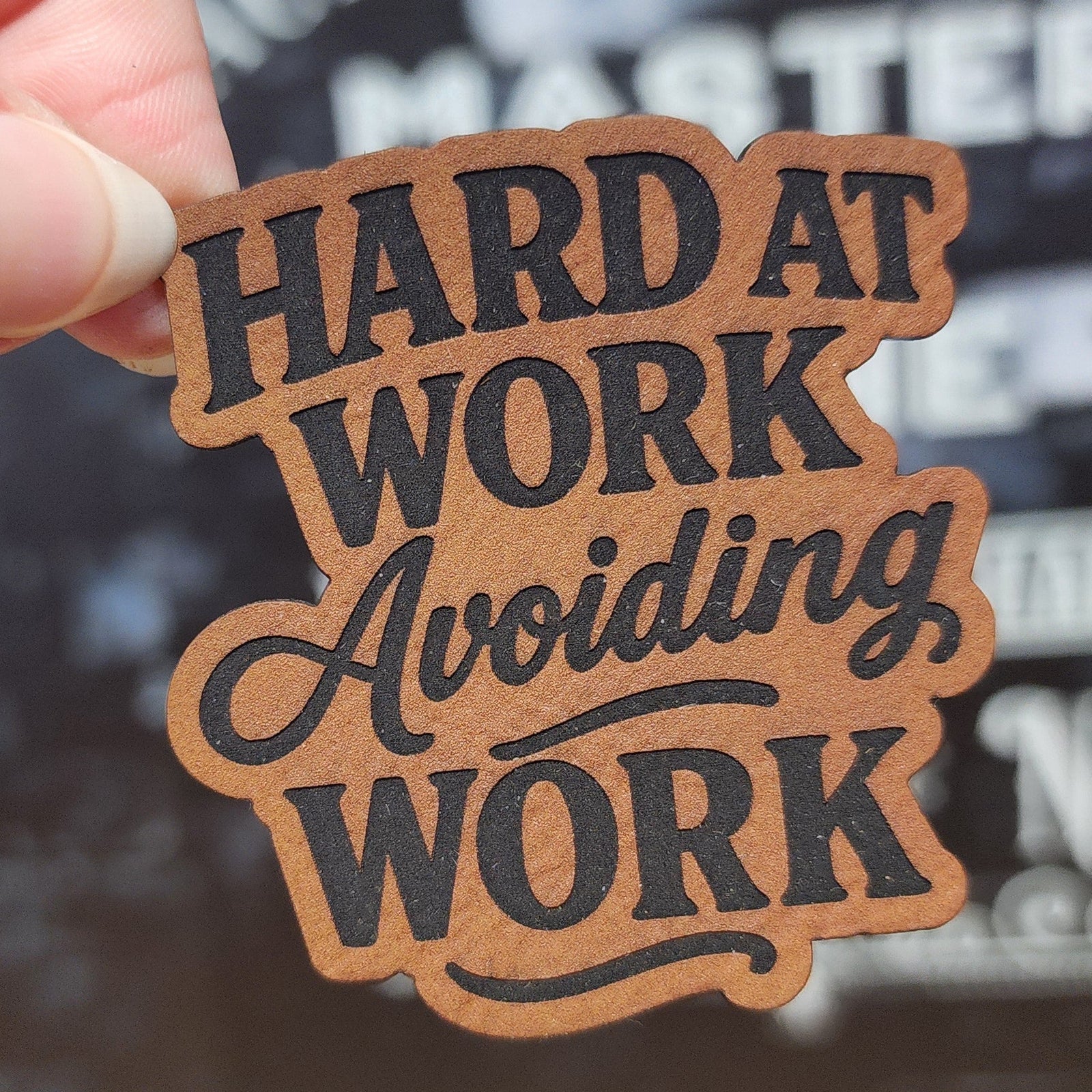 Leatherette hat patch featuring the phrase 'Hard at Work Avoiding Work' perfect for casual caps or work gear.