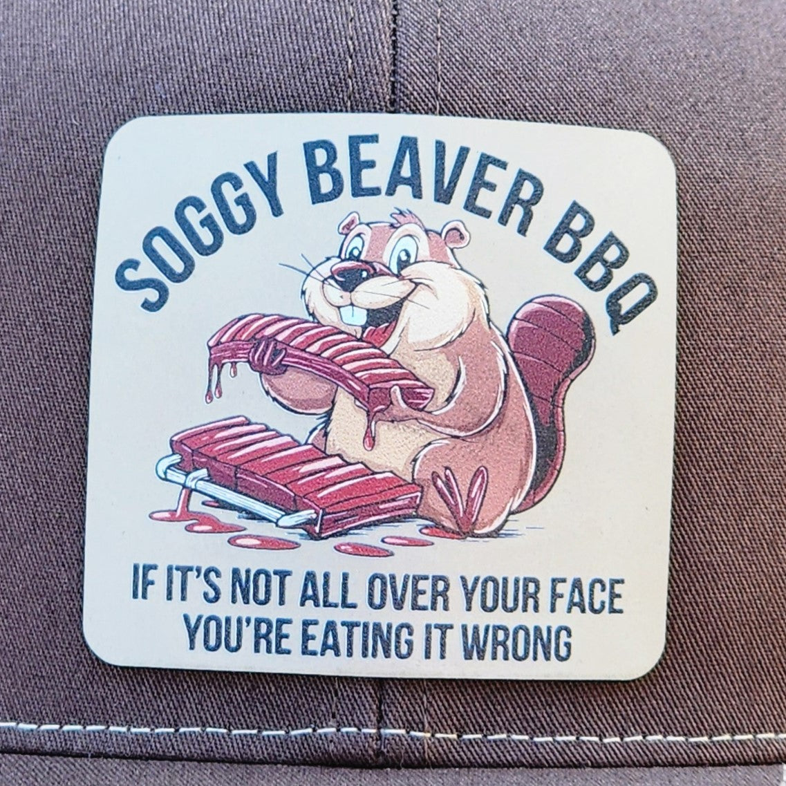 Soggy Beaver BBQ leatherette hat patch featuring a cartoon beaver with BBQ ribs for fun grilling style.