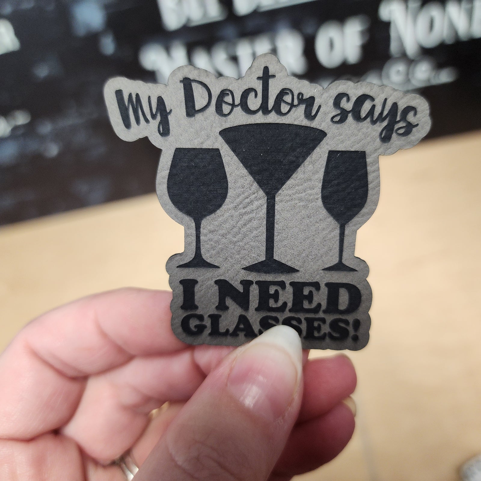 Humorous leatherette hat patch with 'My Doctor Says I Need Glasses!' text and cocktail glasses design for fun gifts.