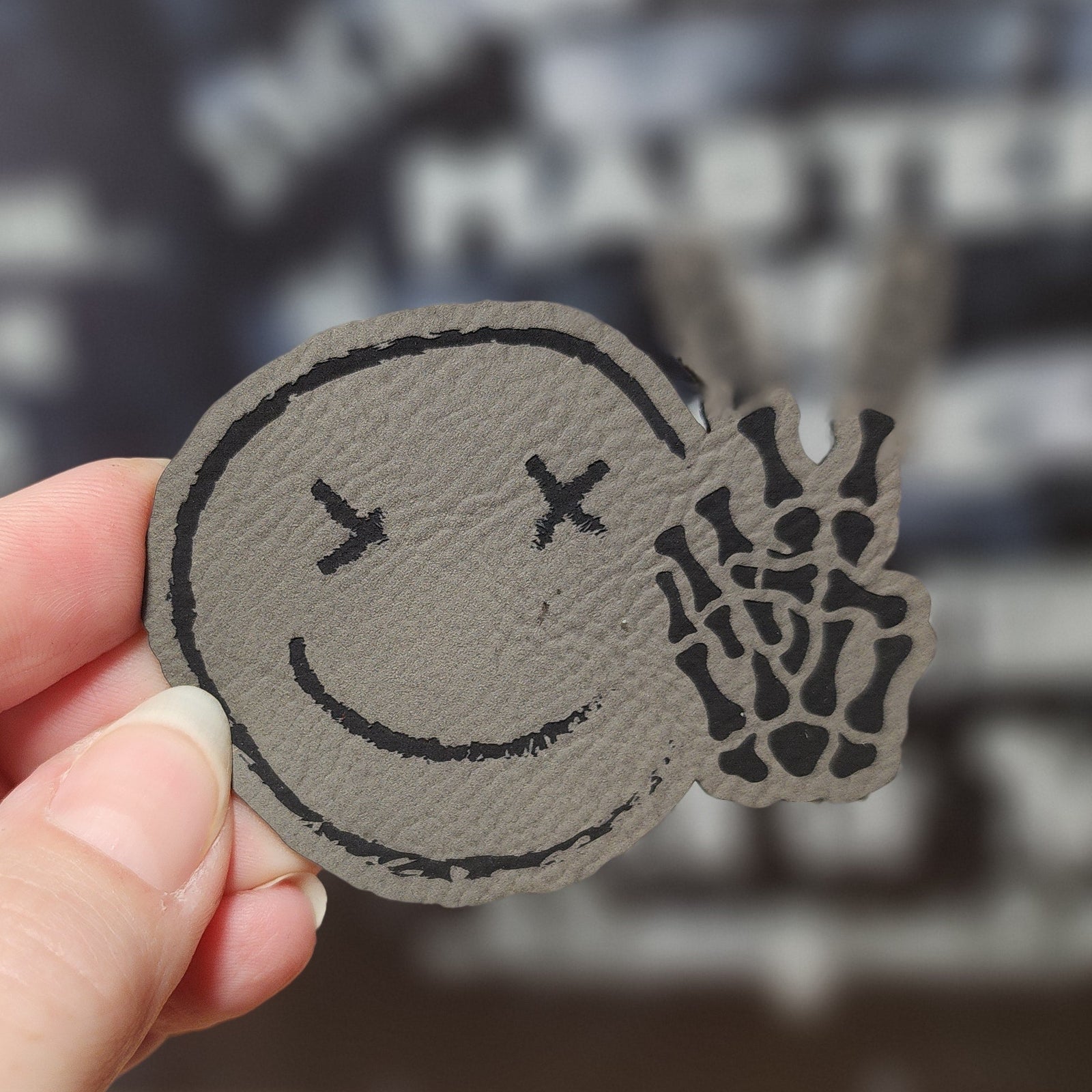 Cool leatherette hat patch with a smiley face and skeleton hand design, perfect for unique accessory lovers.