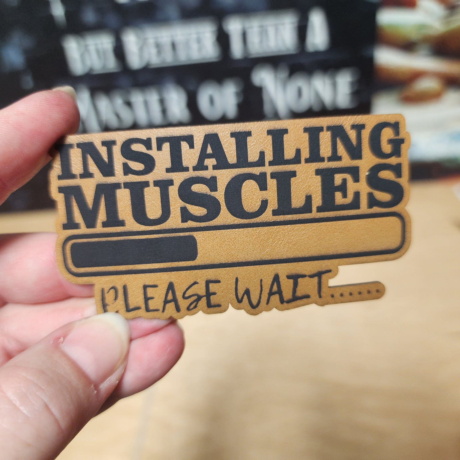 Funny leatherette hat patch saying 'Installing Muscles, Please Wait...' for gym lovers and fitness enthusiasts.