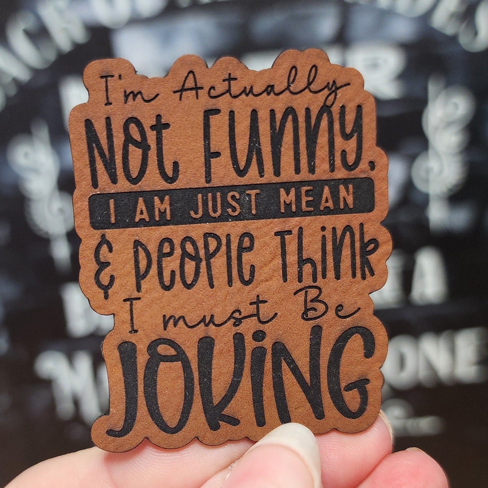 Humorous leatherette hat patch saying 'I'm Actually Not Funny, I Am Just Mean' for witty gift enthusiasts.