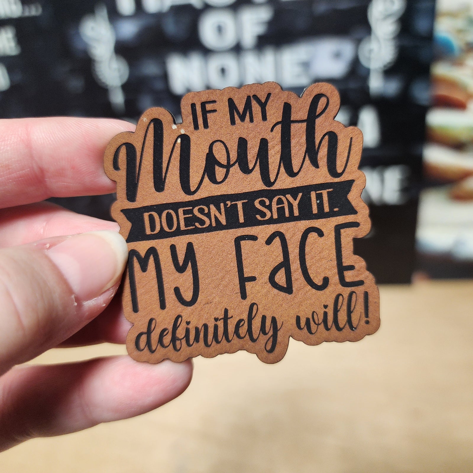 Funny leatherette hat patch saying 'If my mouth doesn't say it, my face definitely will' for witty accessories.
