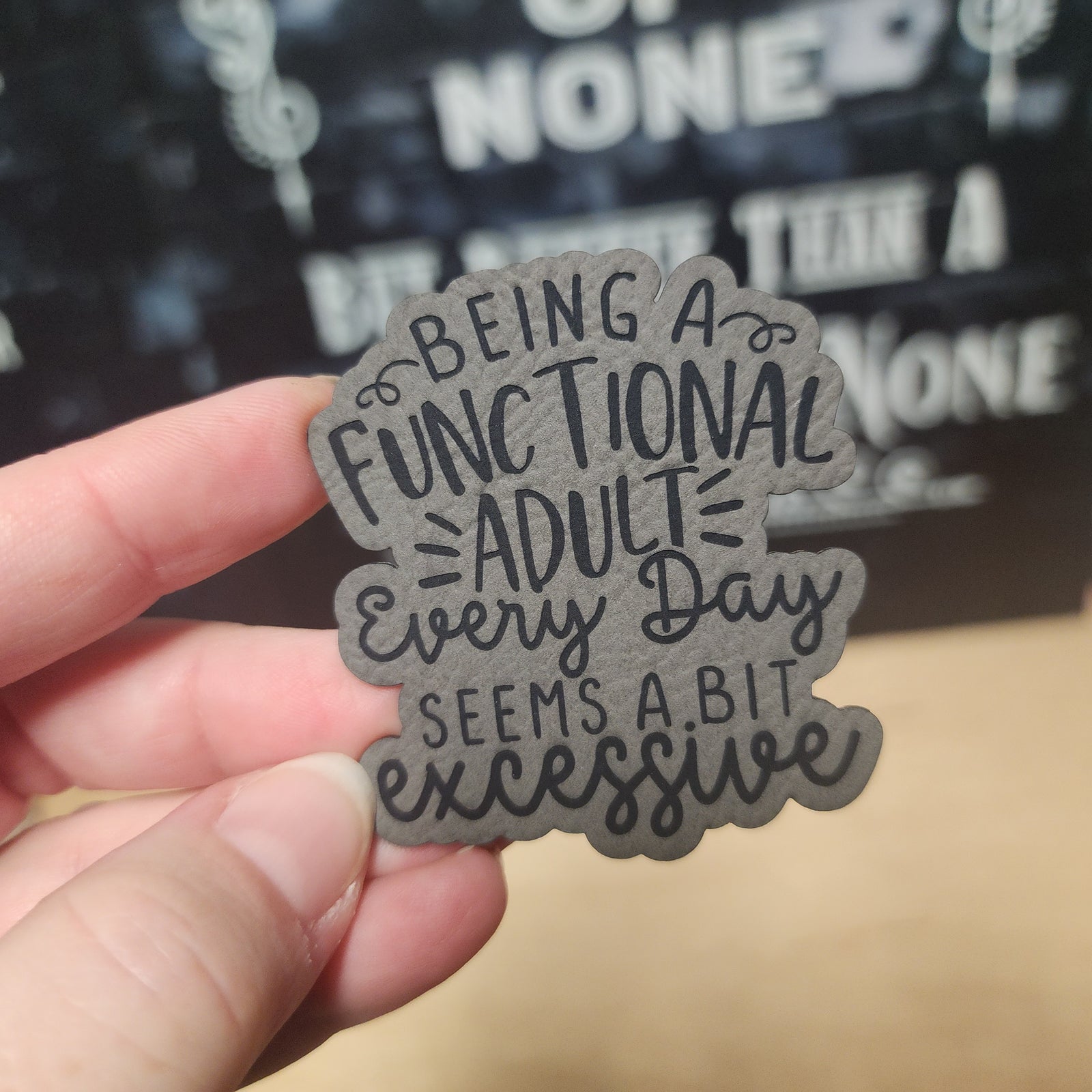 Leatherette hat patch stating 'Being a functional adult every day seems a bit excessive' for quirky accessory lovers.