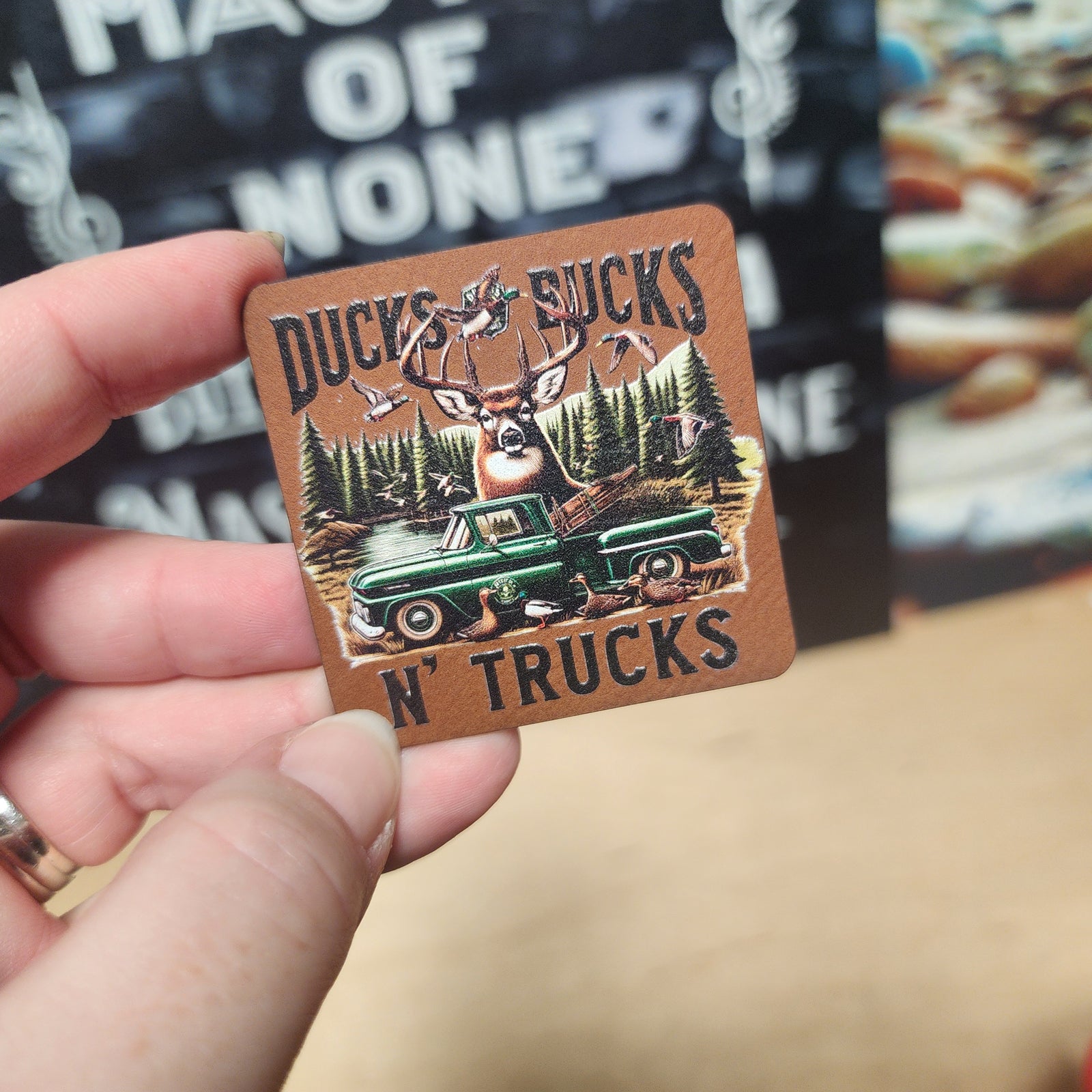 Ducks, Bucks, n' Trucks leatherette hat patch featuring a deer, green truck, and nature scene for outdoor enthusiasts.